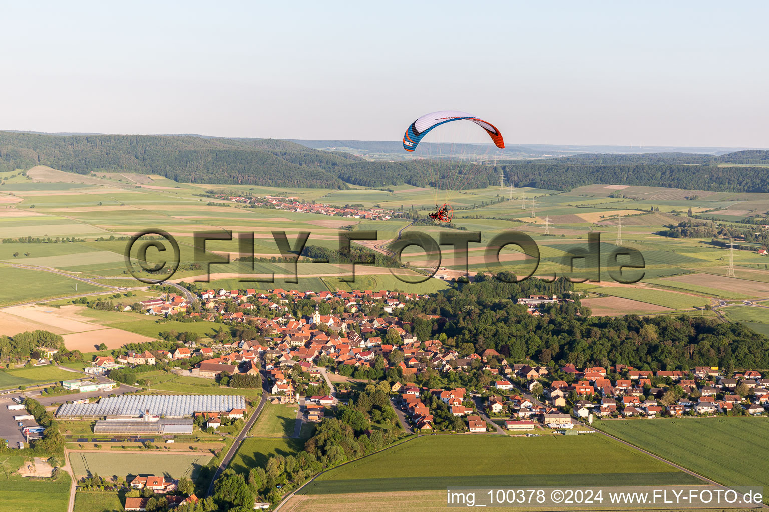 Vue aérienne de Vol en parapente au-dessus d'un village en bordure de champs agricoles et de zones agricoles à Rüdenhausen dans le département Bavière, Allemagne