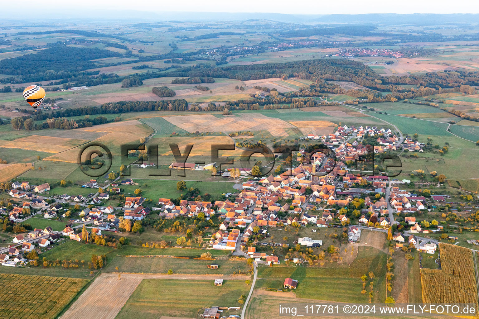 Vue aérienne de Les zones agricoles et les limites des champs entourent la zone d'habitation du village avec une montgolfière à Kindwiller dans le département Bas Rhin, France