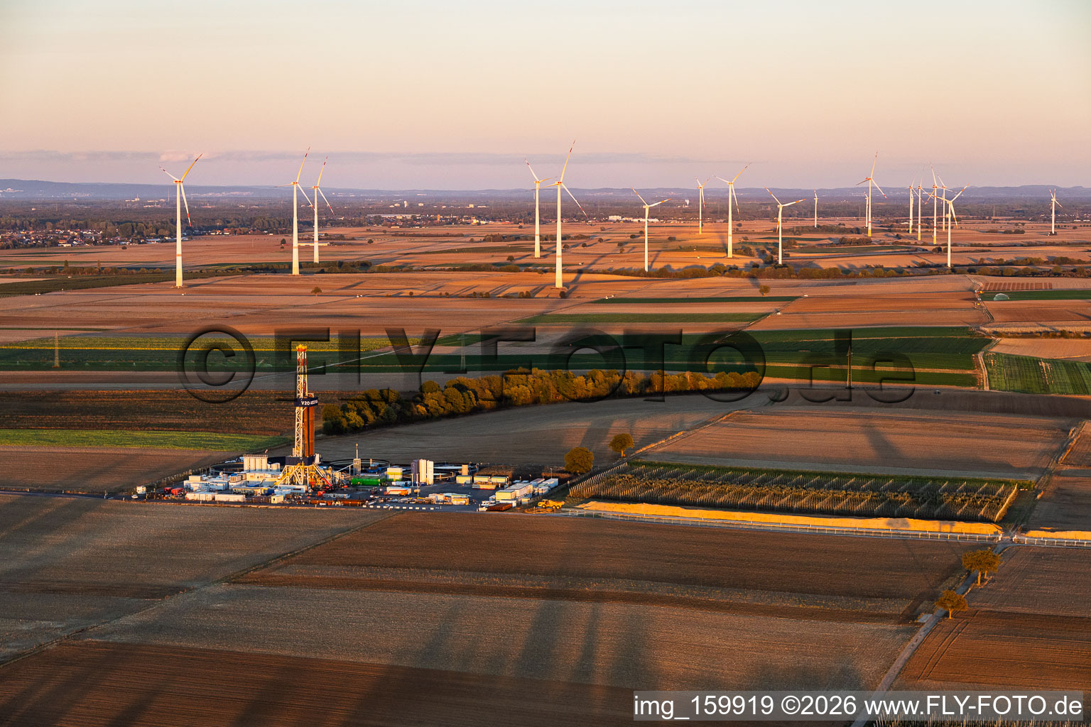 Site de forage profond « Rig V20 - Vercana » (Vulcan Energy) au Schleidberg, avec le parc éolien d'Offenbach en arrière-plan, dans la lumière du soir ; installation destinée à l'exploitation de la géothermie et à l'extraction de lithium à Insheim dans le département Rhénanie-Palatinat, Allemagne
