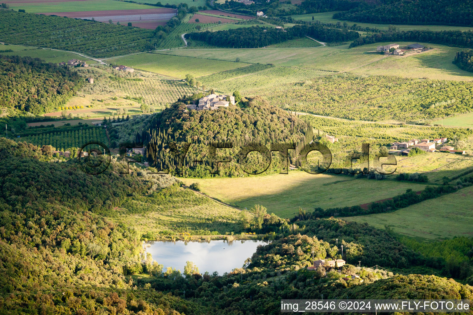 Vue aérienne de Village - vue sur une colline ronde et boisée avec un lac à le quartier Poggio Santa Cecilia in Rapolano Terme dans le département Siena, Italie