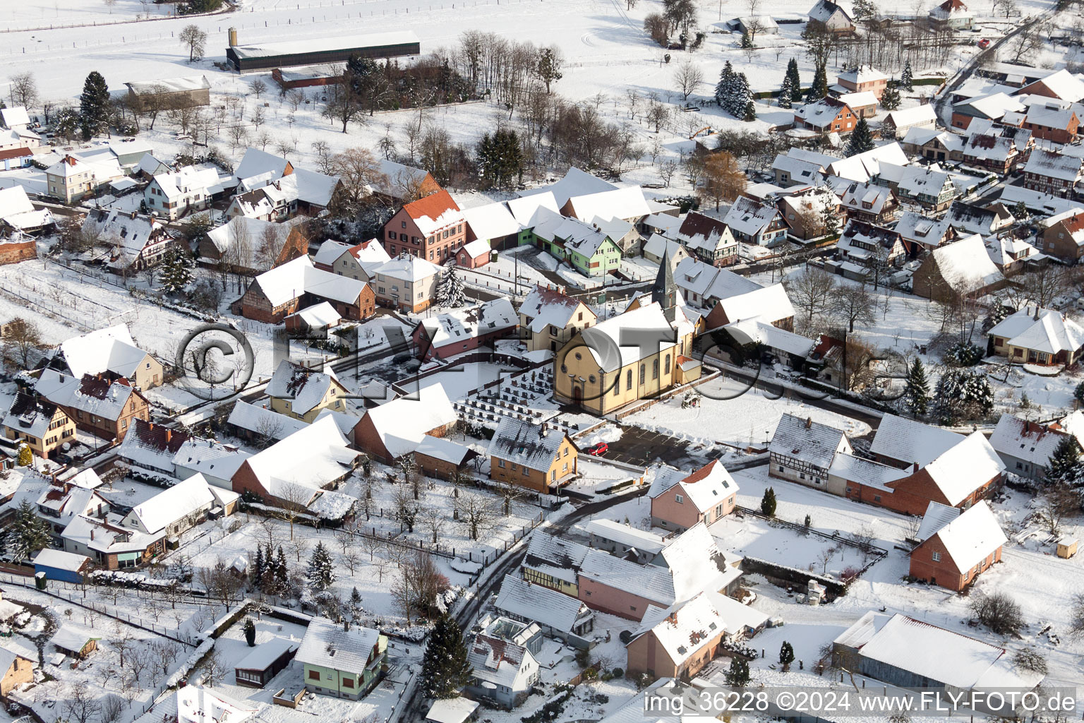 Vue aérienne de Bâtiments d'église enneigés en hiver au centre du village à Oberlauterbach dans le département Bas Rhin, France